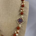 dettaglio collana con pasta corallo rosso e mattonella in ceramica decorata