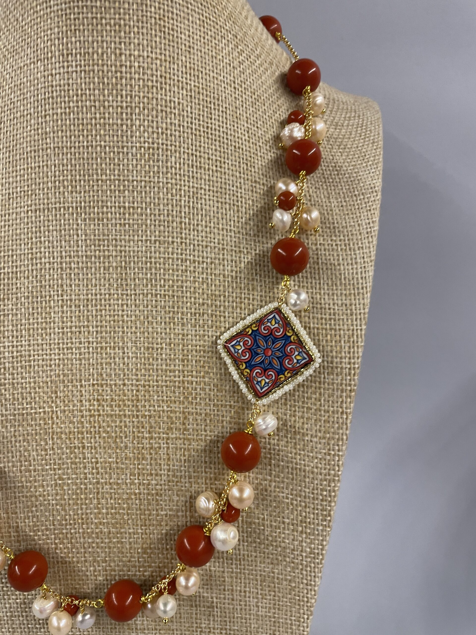 dettaglio collana con pasta corallo rosso e mattonella in ceramica decorata